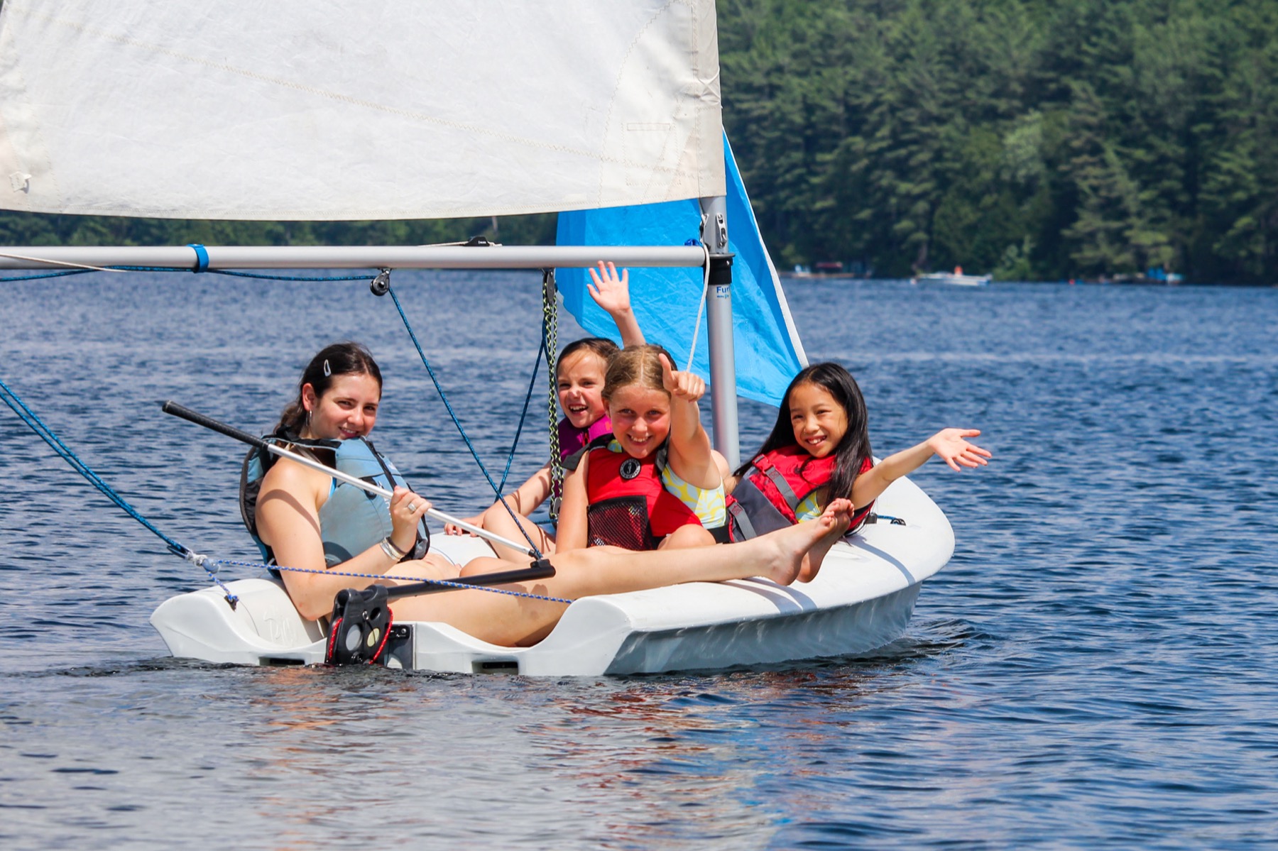 Three campers laughing together on a sailboat on the lake