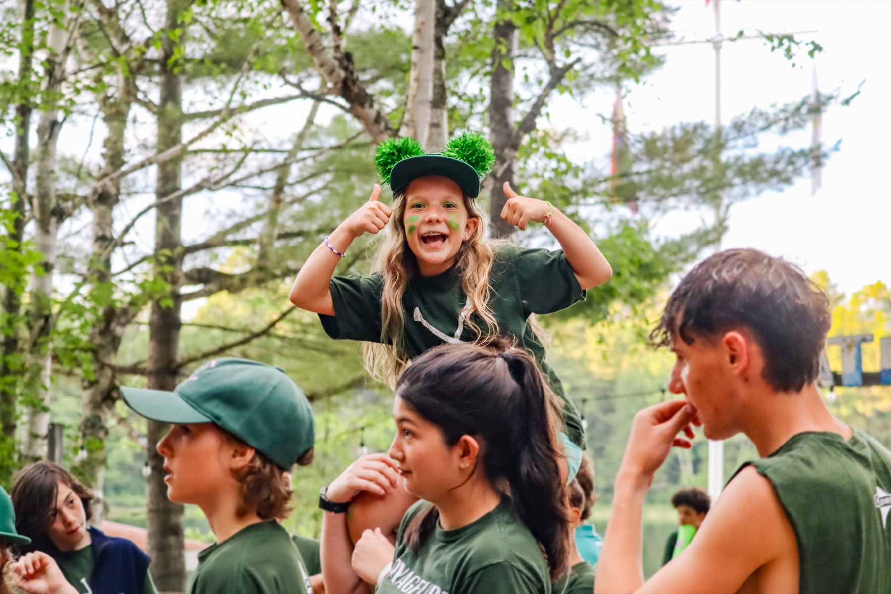 A camper on a friend's shoulders giving two thumbs up at a camp event