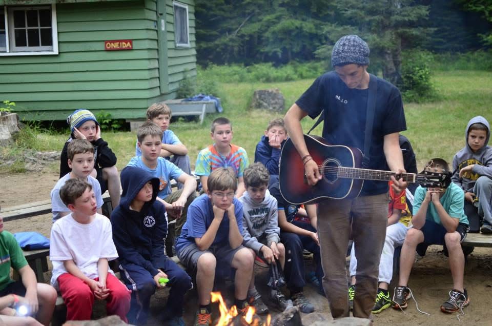 A camp counsellor playing guitar around a campfire with a group of young campers