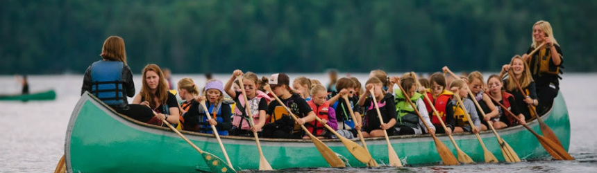 Campers paddling a war canoe across the lake at summer camp